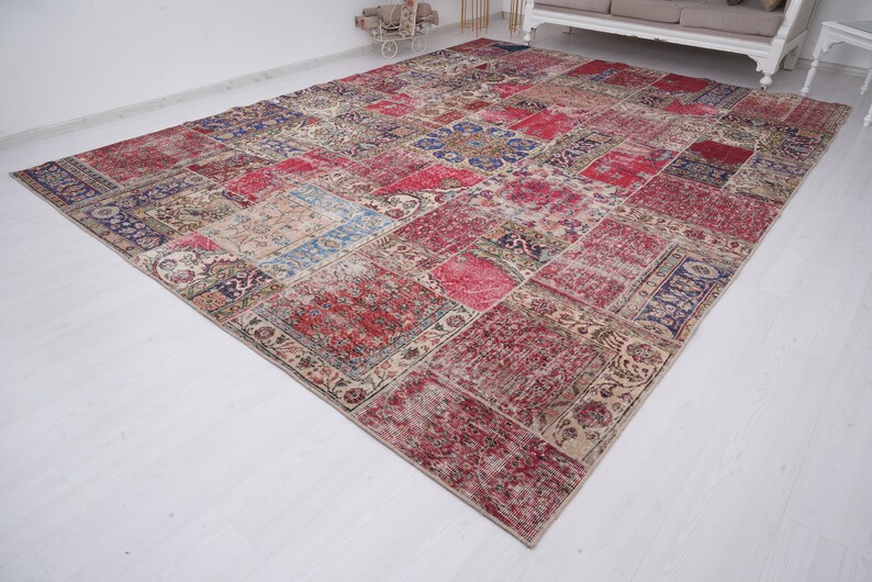 K&ouml;nnte beinhalten: Ein mehrfarbiger Patchwork-Teppich mit verschiedenen floralen und geometrischen Mustern. Der Teppich ist aus einem weichen, gewebten Material gefertigt und hat einen abgenutzten, Vintage-Look.