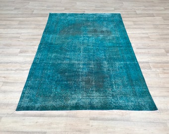 Puede incluir: Una alfombra vintage azul turquesa con un patrón descolorido. La alfombra tiene un borde de flecos blancos.