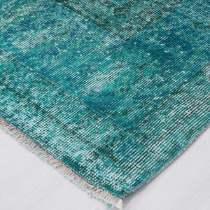 May include: Close-up of a teal blue rug with a faded, distressed pattern. The rug has a white fringe border.