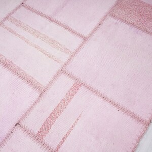 May include: A pink patchwork rug with a textured surface. The rug is made of different pieces of fabric sewn together.