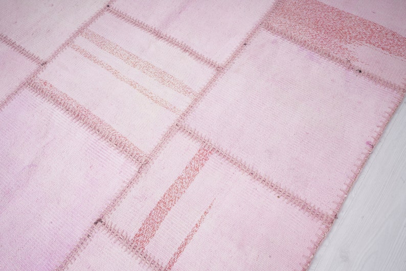 May include: A pink patchwork rug with a textured surface. The rug is made of different pieces of fabric sewn together.