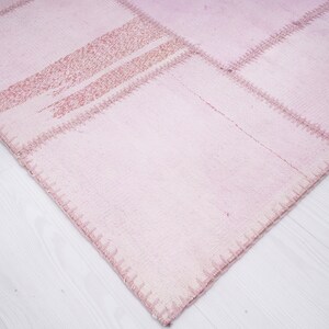 May include: A pink patchwork rug with a textured surface and visible stitching. The rug is made of several different pieces of fabric sewn together.