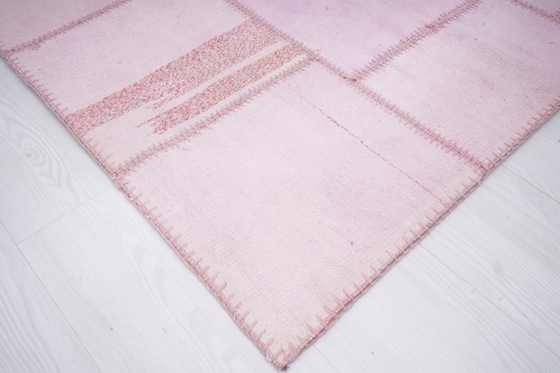 May include: A pink patchwork rug with a textured surface and visible stitching. The rug is made of several different pieces of fabric sewn together.