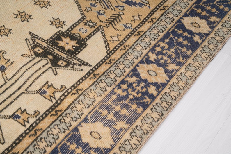 May include: A vintage rug with a cream background and a blue and brown geometric pattern. The rug has a fringe border.
