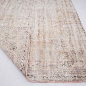 Op de afbeelding: Een vintage tapijt met een vervaagd bloemenpatroon in beige, bruin en roze tinten. Het tapijt heeft een verweerde uitstraling en een gefranst randje.