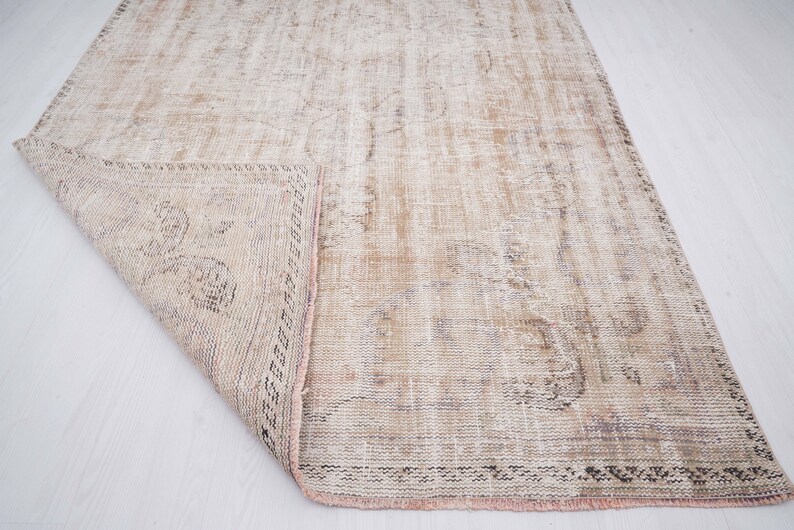 Op de afbeelding: Een vintage tapijt met een vervaagd bloemenpatroon in beige, bruin en roze tinten. Het tapijt heeft een verweerde uitstraling en een gefranst randje.