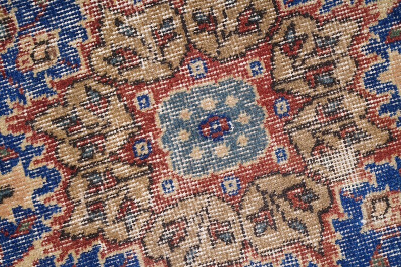 K&ouml;nnte beinhalten: Nahaufnahme eines Vintage-Teppichs mit einem detaillierten Muster in Rot-, Blau- und Beiget&ouml;nen. Der Teppich hat ein zentrales Medaillon mit komplizierten floralen Designs.