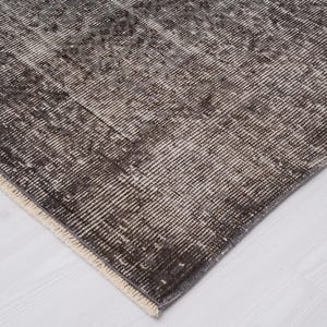 May include: Close-up of a dark gray rug with a white fringe border. The rug has a woven texture and a subtle pattern.