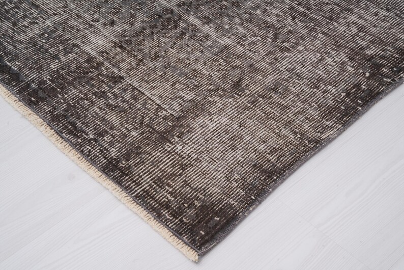May include: Close-up of a dark gray rug with a white fringe border. The rug has a woven texture and a subtle pattern.