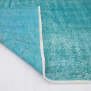May include: Close-up of a teal blue rug with a white fringe. The rug is folded over, showing the underside of the fabric.