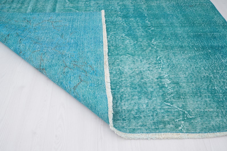 May include: Close-up of a teal blue rug with a white fringe. The rug is folded over, showing the underside of the fabric.