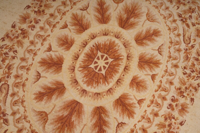 Puede incluir: Una alfombra beige y marr&oacute;n con un patr&oacute;n circular de hojas y flores. La alfombra tiene un dise&ntilde;o detallado y una est&eacute;tica vintage.