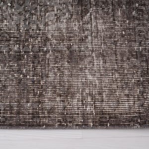 May include: Close-up of a dark gray rug with a subtle pattern. The rug has a fringed edge and is made of a soft, woven material.