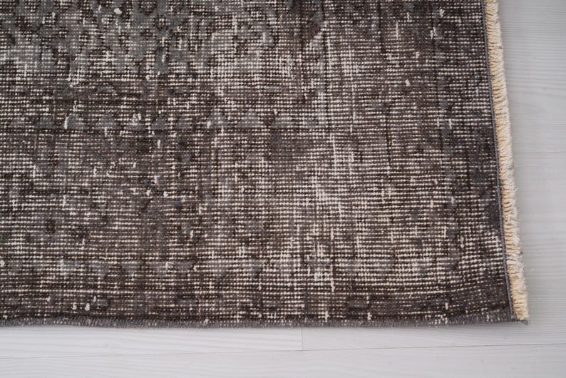 May include: Close-up of a dark gray rug with a subtle pattern. The rug has a fringed edge and is made of a soft, woven material.