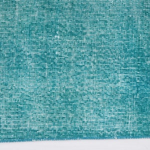 May include: A close-up of a teal blue rug with a woven texture. The rug has a white fringe along the edges.