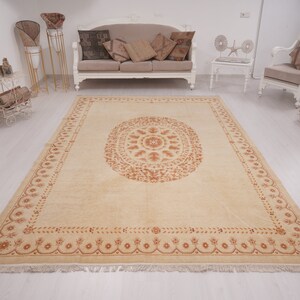 Puede incluir: Una alfombra beige con un gran dise&ntilde;o de medall&oacute;n central de color naranja-marr&oacute;n intrincado. La alfombra tiene un borde con flecos.