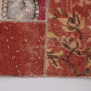 Puede incluir: Una alfombra de retazos con secciones rectangulares de tela tejida. Una secci&oacute;n muestra un fondo rojo intenso con un patr&oacute;n floral en amarillo y marr&oacute;n apagados, mientras que otra secci&oacute;n muestra un tejido rojo texturizado con motas blancas.