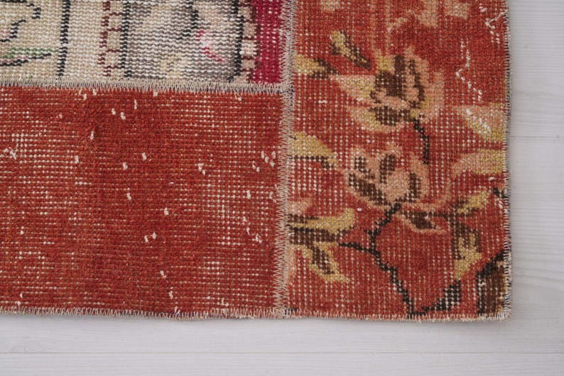 Puede incluir: Una alfombra de retazos con secciones rectangulares de tela tejida. Una secci&oacute;n muestra un fondo rojo intenso con un patr&oacute;n floral en amarillo y marr&oacute;n apagados, mientras que otra secci&oacute;n muestra un tejido rojo texturizado con motas blancas.