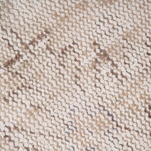 Op de afbeelding: Close-up van een geweven tapijt met een beige en bruin patroon. Het tapijt heeft een textuur en een diagonale weving.