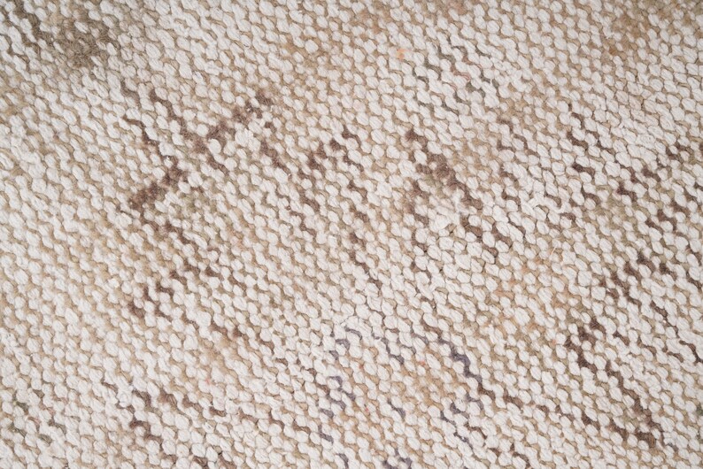 Op de afbeelding: Close-up van een geweven tapijt met een beige en bruin patroon. Het tapijt heeft een textuur en een diagonale weving.