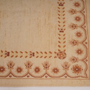 Puede incluir: Una alfombra beige con un borde de patr&oacute;n floral marr&oacute;n. La alfombra tiene flecos en el lado derecho.