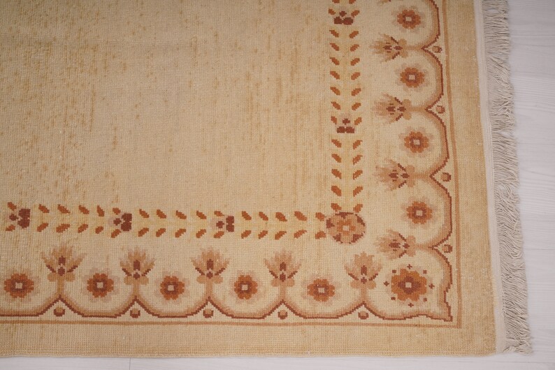 Puede incluir: Una alfombra beige con un borde de patr&oacute;n floral marr&oacute;n. La alfombra tiene flecos en el lado derecho.