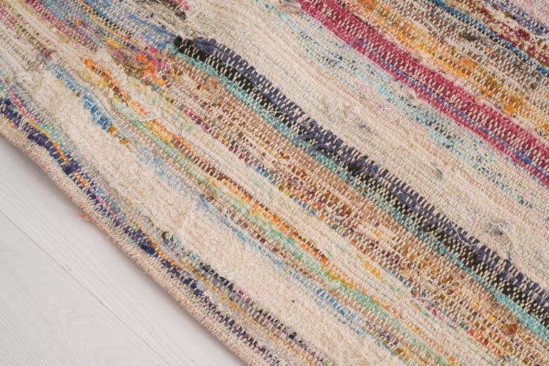 May include: A woven area rug featuring a multi-colored striped pattern with bands of pink, blue, orange, yellow, and dark green interspersed with a neutral off-white base. The textile displays a textured, hand-loomed appearance with visible fibers.
