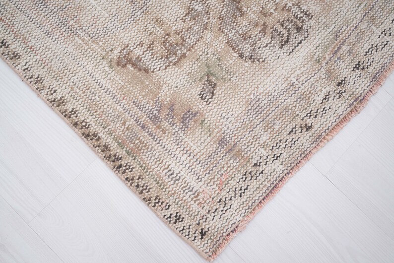 Op de afbeelding: Close-up van een geweven beige en bruin tapijt met een roze franje. Het tapijt heeft een subtiel patroon en een verweerde look.
