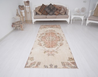 May include: A rectangular, vintage-style rug with a central medallion design in shades of peach, cream, and brown. The rug features floral and botanical patterns along the borders and within the central design. The rug is placed on a white floor.