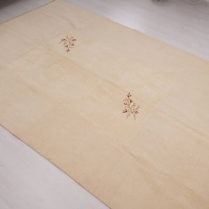 Pu&ograve; includere: Un tappeto color crema con una texture sottile e due disegni floreali ricamati in marrone.