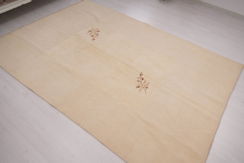 Pu&ograve; includere: Un tappeto color crema con una texture sottile e due disegni floreali ricamati in marrone.