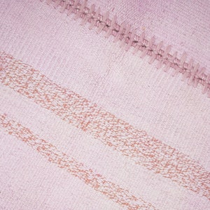 May include: A pink woven rug with two horizontal stripes of a darker pink color. The rug has a fringe border.