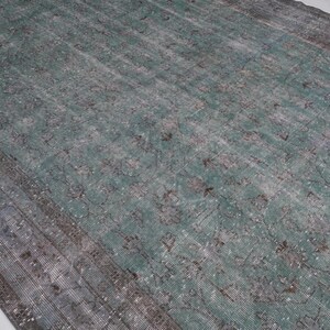 May include: A vintage rug with a faded teal and gray color scheme. The rug has a distressed look with a subtle pattern throughout.