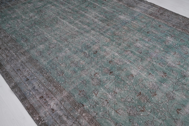 May include: A vintage rug with a faded teal and gray color scheme. The rug has a distressed look with a subtle pattern throughout.