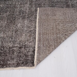 May include: Close-up of the back side of a dark gray rug with a white fringe. The rug is folded in half, revealing the underside, which is a lighter shade of gray.