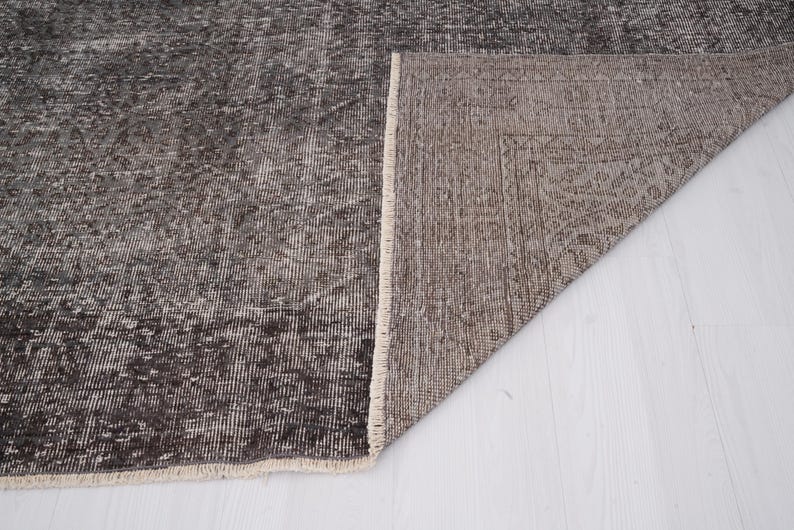 May include: Close-up of the back side of a dark gray rug with a white fringe. The rug is folded in half, revealing the underside, which is a lighter shade of gray.