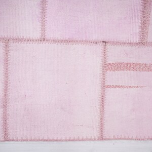 May include: A pink patchwork rug with a stitched design. The rug is made of several pieces of fabric sewn together.
