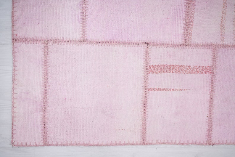 May include: A pink patchwork rug with a stitched design. The rug is made of several pieces of fabric sewn together.
