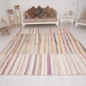 May include: A rectangular area rug featuring a multi-colored striped pattern with a palette of cream, beige, pink, yellow, and dark brown tones. The rug displays a woven texture with vertical lines running across the entire surface of the piece.