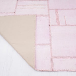 May include: A pink patchwork rug with a beige backing. The rug is made of different pieces of fabric sewn together.