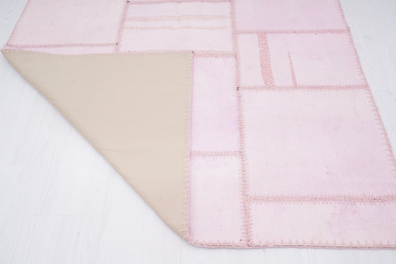 May include: A pink patchwork rug with a beige backing. The rug is made of different pieces of fabric sewn together.