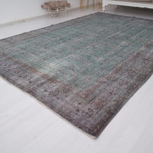 May include: A vintage rug with a faded green center and a brown border. The rug has a distressed look and is made of wool.
