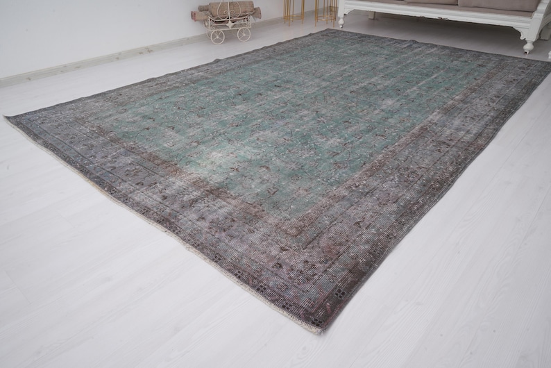 May include: A vintage rug with a faded green center and a brown border. The rug has a distressed look and is made of wool.