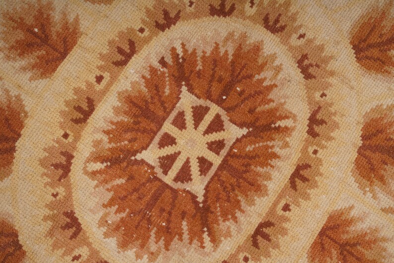 Puede incluir: Primer plano de una alfombra de color beige y marr&oacute;n con un dise&ntilde;o central de un sol estilizado.