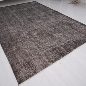 May include: A dark gray vintage rug with a faded, distressed look. The rug has a subtle pattern and a soft, worn texture.