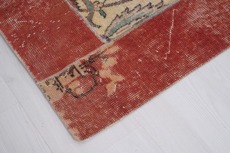 Puede incluir: Una alfombra tejida que presenta un borde rojo intenso prominente con una textura desgastada y descolorida. La secci&oacute;n central muestra un campo de color crema adornado con intrincados patrones florales en tonos apagados de azul, verde y bronceado, mostrando signos de desgaste.