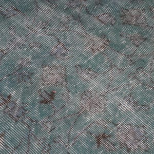May include: A close-up of a teal blue rug with a faded, distressed pattern. The rug has a subtle, woven texture and a vintage look.