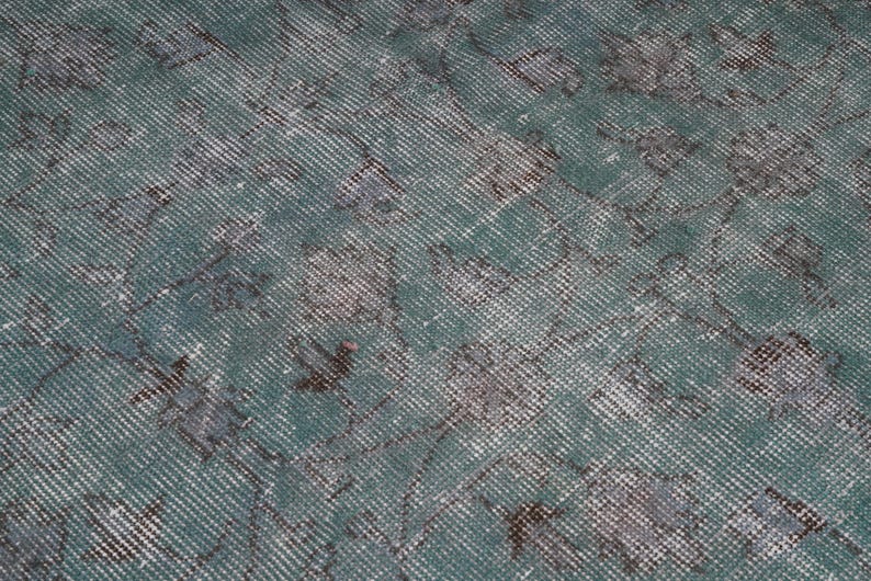 May include: A close-up of a teal blue rug with a faded, distressed pattern. The rug has a subtle, woven texture and a vintage look.