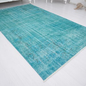May include: A turquoise blue vintage rug with a faded pattern. The rug has a white fringe border.