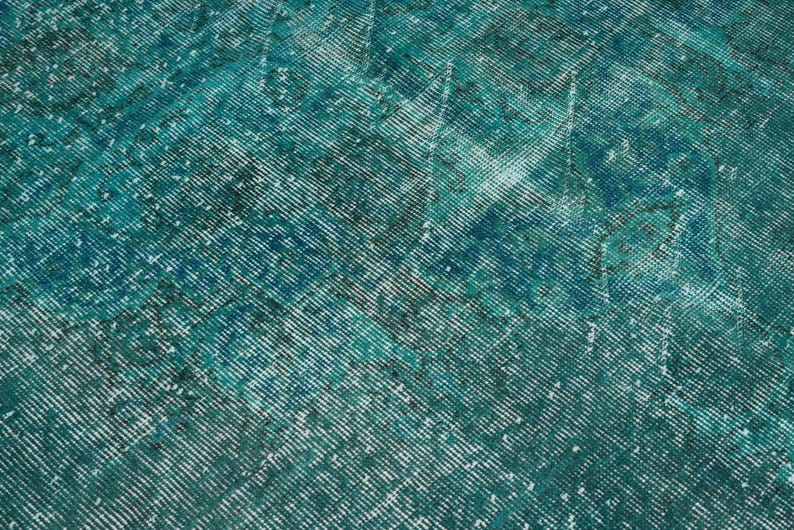 May include: A teal blue rug with a faded, distressed pattern. The rug has a textured, woven surface.